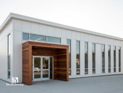 Modern commercial steel building with tall vertical windows and a wooden entrance feature. Ideal for offices, showrooms, or business spaces with a sleek contemporary look.