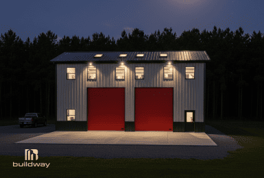 Two-story steel workshop with red roll-up doors and exterior lighting at night, built for heavy-duty use, storage, and flexible workspace needs.