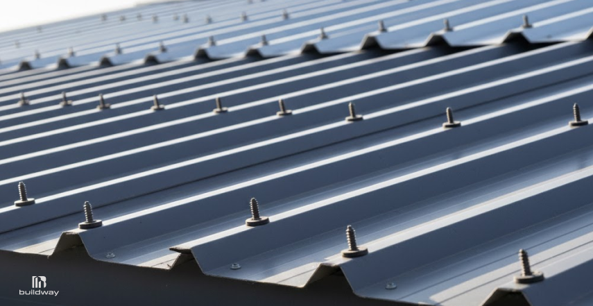 Close-up of an exposed fastener metal roof system, showing rows of steel panels secured with visible screws and washers aligned across the roof surface.