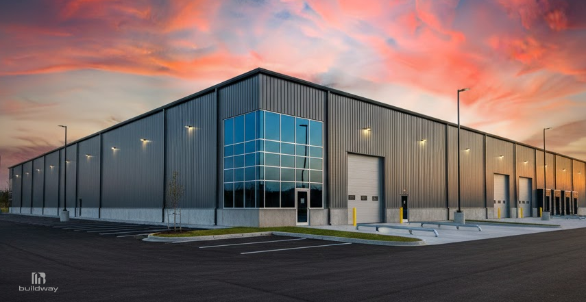 Modern steel warehouse with metal siding, large glass windows, and multiple loading bay doors, set in a clean industrial lot at sunset.