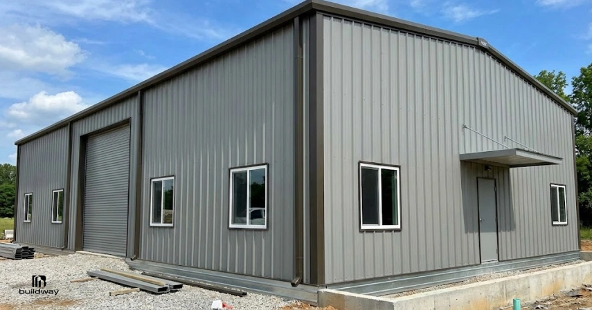 Completed steel building with windows, a roll-up door, and a side entrance, shown on a gravel lot.